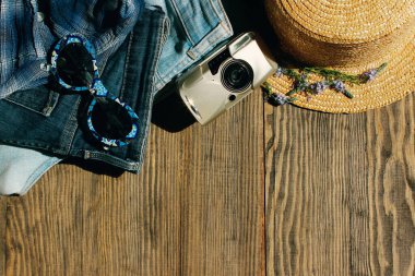 Kadın kıyafetleri, üst manzara, düz yatak. Yaz şapkası, kadın kotu, güneş gözlüğü ve küçük kamera, üst manzara. Alışveriş, seyahat, tatil konsepti. Kadın fotoğrafçı işleri. Yaz ögeleri kümesi.