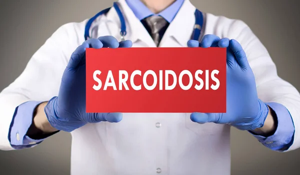 Las manos del doctor en guantes azules muestran la palabra sarcoidosis. Concepto médico . —  Fotos de Stock