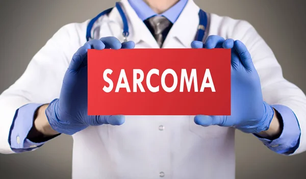 Le mani del dottore con i guanti blu mostrano la parola sarcoma. Concetto medico. — Foto Stock