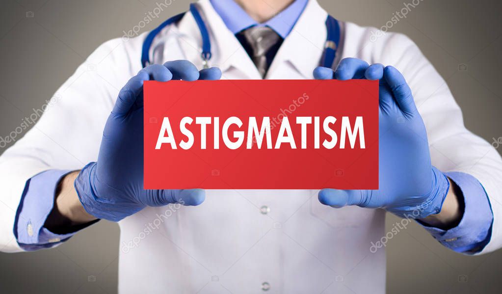 Doctor's hands in blue gloves shows the word astigmatism. Medical concept.