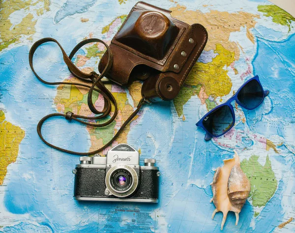 Accessories of a traveler on a background map of the world with a camera, sunglasses and shell — Stock Photo, Image