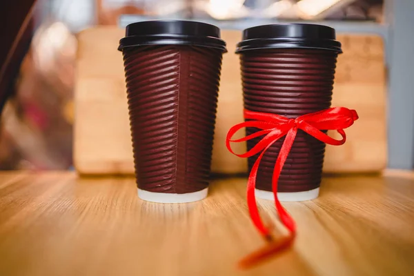 Two plastic cups of coffee with a lid on a wooden background