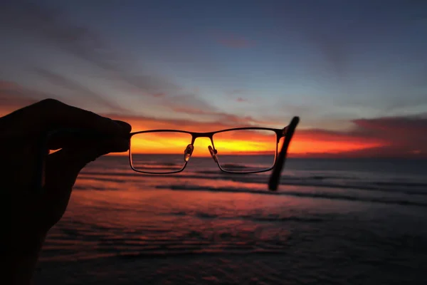 Puesta de sol y océano a través de gafas en una mano Fotos De Stock