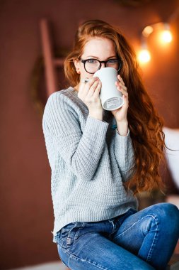 Noel ile odada oturup çay içme uzun kızıl saçlı genç gülümseyen kız arka plan üzerinde ışıklar