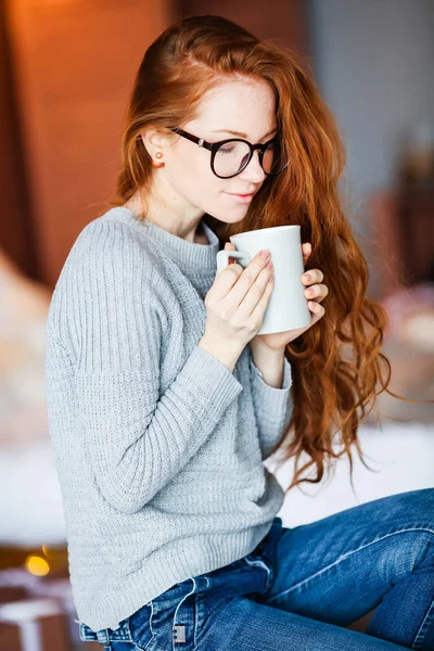 クリスマスに座ってお茶のカップを保持している赤髪少女の部屋で飾った — ストック写真