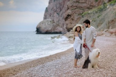 tüylü köpekle kumsalda yürüyen genç çiftin tam uzunlukta