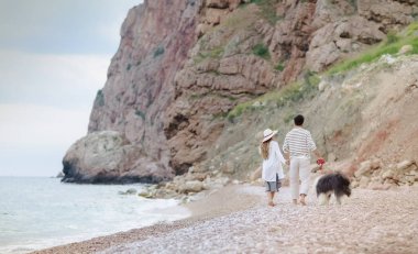 Kumsalda, arkadan görünüm ile tüylü köpek yürüyen genç çiftin tam uzunlukta