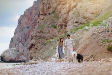 tüylü köpekle kumsalda yürüyen genç çiftin tam uzunlukta