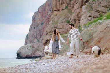 tüylü köpekle kumsalda yürüyen genç çiftin tam uzunlukta