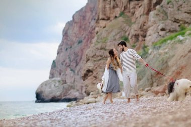 tüylü köpekle kumsalda yürüyen genç çiftin tam uzunlukta