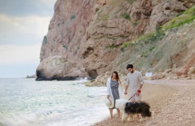 mutlu genç çift ile tüylü köpek Sahilde yürüyüş elele