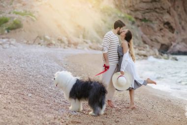 Sahilde tüylü köpek ile ayakta ve öpüşme genç çiftin tam uzunlukta