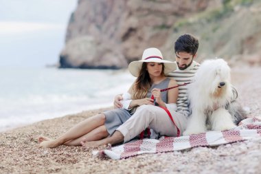 tüylü köpekle ekose sahilde oturup istirahat aşık genç Çift