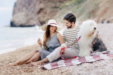 Genç çift ekose plaj ve gülümseyerek oturan tüylü köpek ile dinlenme aşık 