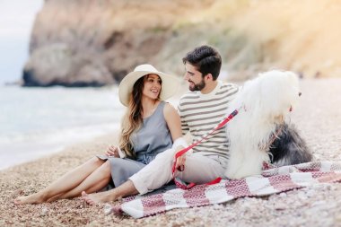 Genç çift ekose plaj ve gülümseyen birbirine bakarak otururken tüylü köpek ile dinlenme aşık