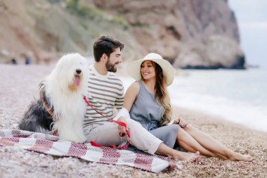 Genç çift ekose plaj ve gülümseyen birbirine bakarak otururken tüylü köpek ile dinlenme aşık