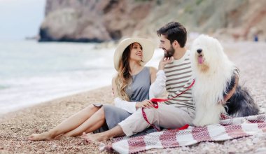 Genç çift ekose plaj ve gülümseyen birbirine bakarak otururken tüylü köpek ile dinlenme aşık