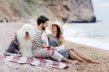 Genç çift ekose plaj ve gülümseyen birbirine bakarak otururken tüylü köpek ile dinlenme aşık