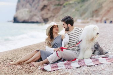 Genç çift ekose plaj ve gülümseyen birbirine bakarak otururken tüylü köpek ile dinlenme aşık