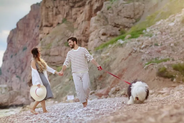 ビーチでふわふわの犬を連れて歩いて手を繋いでいるスタイリッシュな幸せなカップル — ストック写真