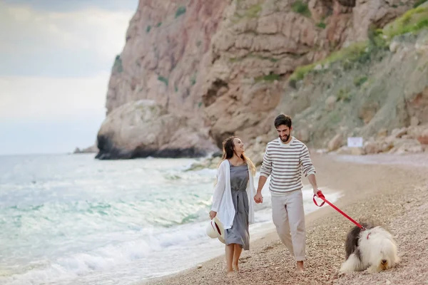 Happy Νεαρό Ζευγάρι Κρατώντας Χέρια Περπατώντας Αφράτο Σκύλο Στην Παραλία — Φωτογραφία Αρχείου