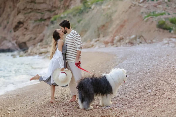 Sahilde tüylü köpek ile ayakta ve öpüşme genç çiftin tam uzunlukta