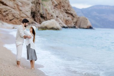 Beyaz şapkalı erkek arkadaşıyla kumsalda yalınayak ayakta sarılma genç gülümseyen kız