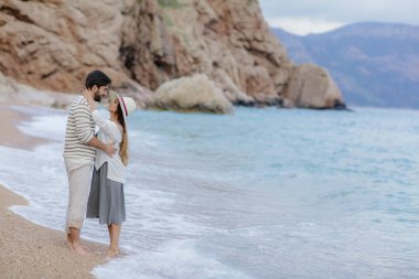 şık genç çift aşık ayakta kumsalda yalınayak cliff ve arka plan, tam uzunlukta dağda ile sarılma