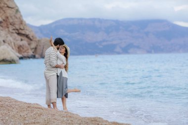 mutlu adam arka plan, tam uzunlukta cliff ve dağ ile yalınayak kumsalda üzerinde duran güzel onun gülümseyen kadın kucaklayan