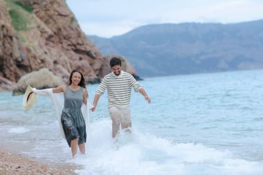 mutlu çift ıslak giysileri el ele tutuşarak deniz kıyısında çalıştıran gülüyor