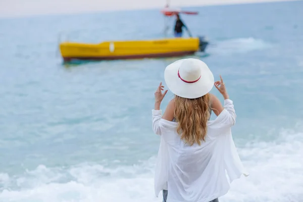 ビーチ ビューに戻って 海で泳いでボートを見て上に立っている長い巻き毛を持つ若い女性 — ストック写真