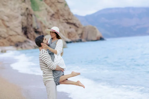 海の岸に立っているをかなり笑っている女の子を持ち上げる幸せなハンサムな男 — ストック写真