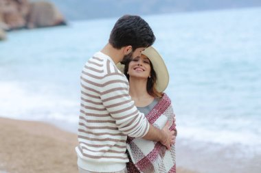 şapkalı güzel kadını kucaklayan ve onu deniz ve dağ zemin üzerine ekose konumu olan kapsayan yakışıklı adam