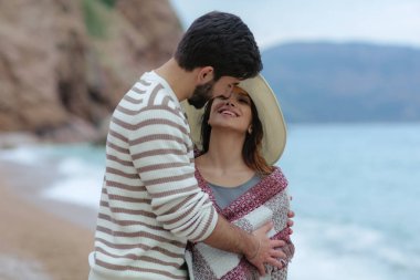 şapkalı güzel kadını kucaklayan ve onu deniz ve dağ zemin üzerine ekose konumu olan kapsayan yakışıklı adam