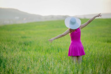 mor elbise ve beyaz şapka Dağları üzerinde arka plan, arkadan görünüm ile yeşil alan üzerinde yürüme genç kadın