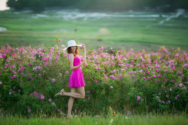 紫色のドレスと楽しい時を過す白い帽子の若い女性の完全な長さの花ポーズ — ストック写真