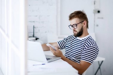 genç yakışıklı işadamı ofis masasında otururken dizüstü bilgisayar üzerinde çalışan telefon kullanma