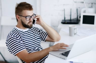 genç yakışıklı işadamı ofis masasında otururken dizüstü bilgisayar üzerinde çalışan telefon konuşma