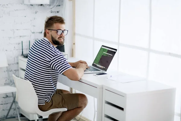 年轻英俊的生意人打字在笔记本电脑坐在办公桌在现代办公室 — 图库照片