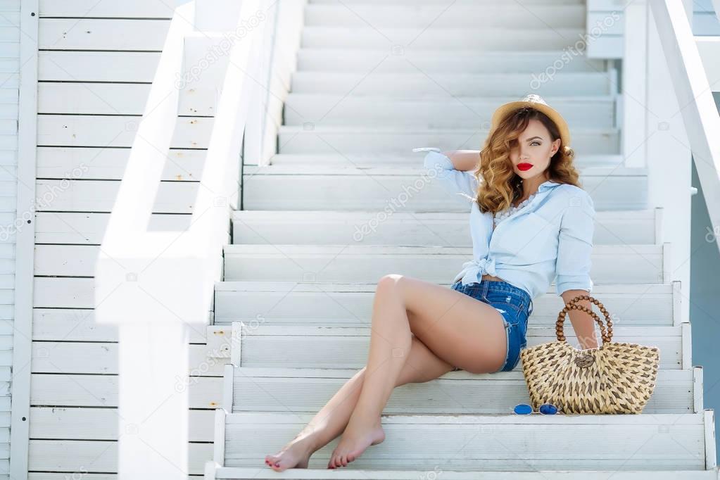 stylish woman sitting on stairs in straw hat with bag, full length