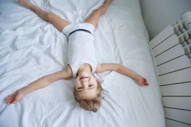 küçük çocuğa eğleniyor görüntülemek yukarıdan beyaz yatakta yatarken 