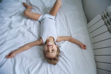 küçük çocuğa eğleniyor görüntülemek yukarıdan beyaz yatakta yatarken 