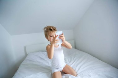 küçük çocuk Smartphone'da oynayan beyaz yatakta otururken yukarıdan görüntüleyin