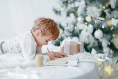 Beyaz kanepe Noel ağacının altında yatan ve dilek listesi yapma küçük çocuk