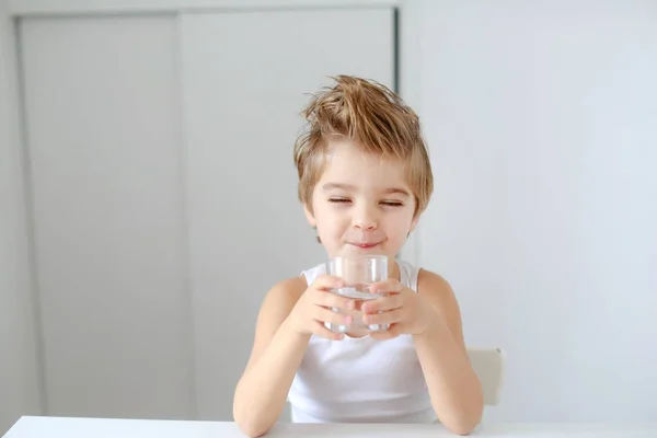 Divertido Niño Sosteniendo Vaso Agua Sentado Mesa Blanca — Foto de Stock