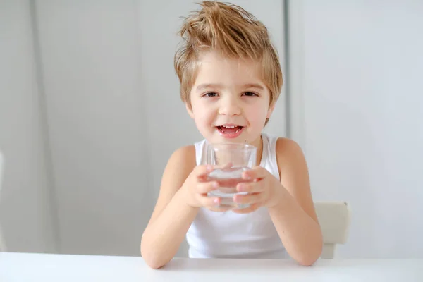 Divertido Niño Sosteniendo Vaso Agua Sentado Mesa Blanca — Foto de Stock