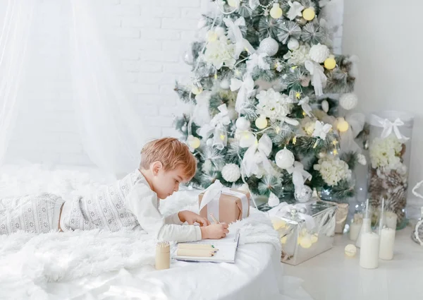 Kleine Jongen Liggend Witte Bed Buurt Van Kerstboom Schrijven Notebook — Stockfoto