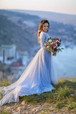 açık havada poz çiçek buketi tutan muhteşem mavi elbiseli genç güzel gelin 