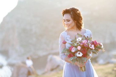 açık havada poz çiçek buketi tutan muhteşem mavi elbiseli genç güzel gelin 