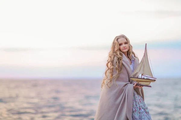 Vacker Blond Flicka Holding Träleksak Fartyget Stående Stranden Vid Solnedgången — Stockfoto